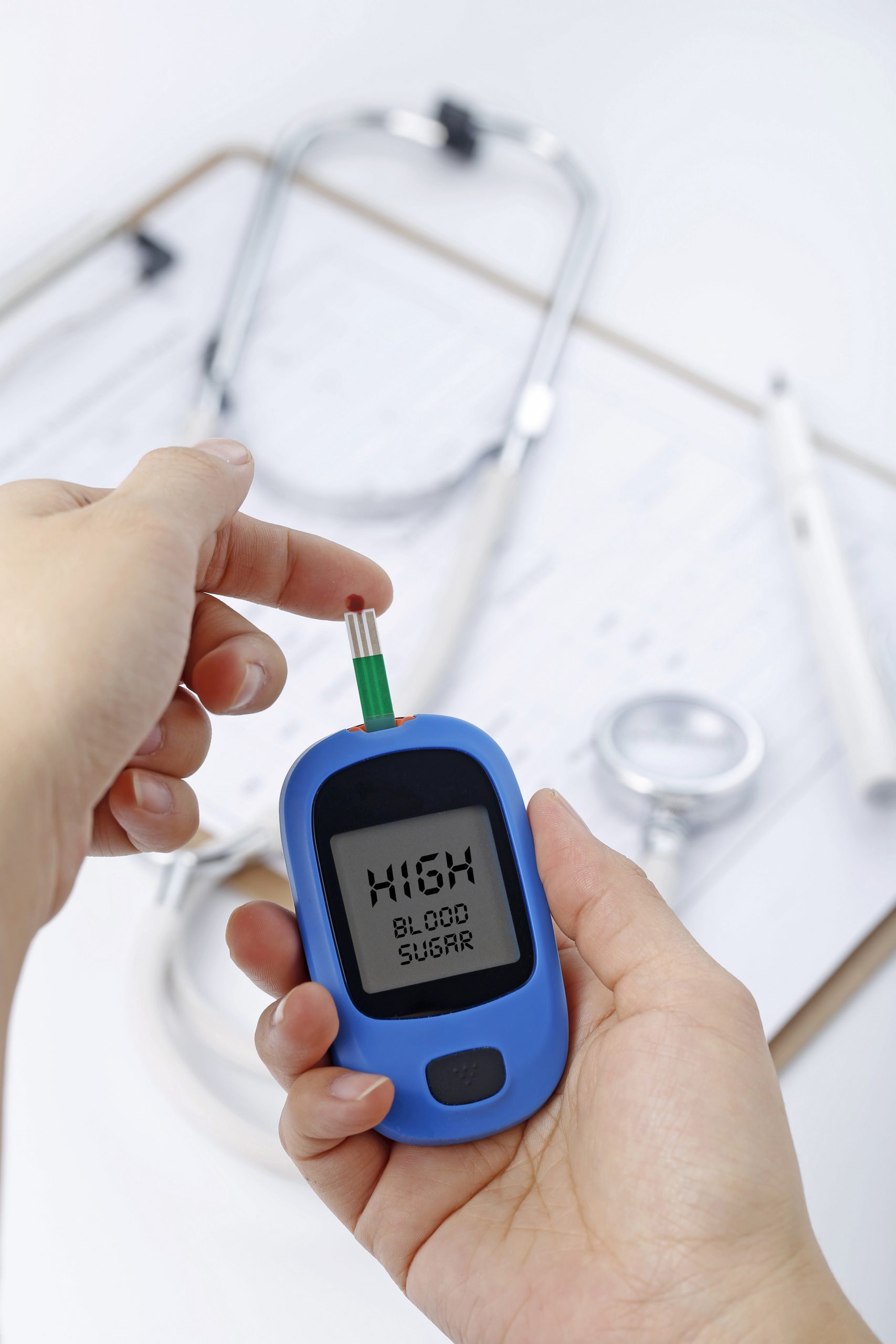 Hand holding a blood glucose meter measuring blood sugar, the background is a stethoscope and chart file Hand holding a blood glucose meter measuring blood sugar, the background is a stethoscope and chart file